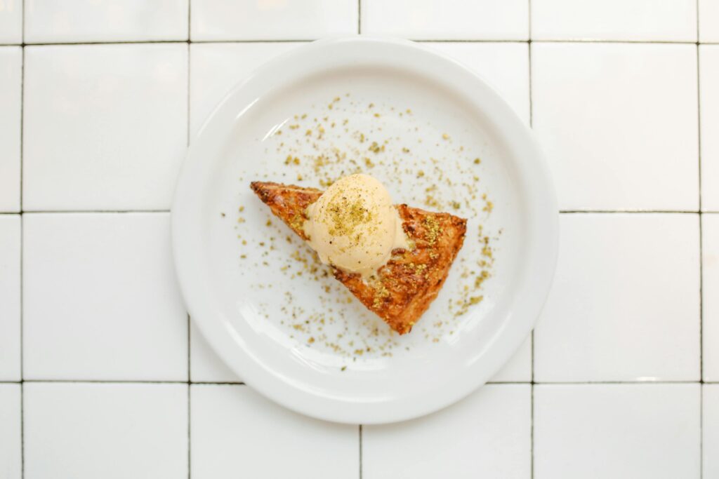 Slice of baklava with ice cream on a white plate, adorned with finely ground nuts.